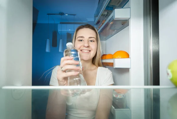 Vackra leende kvinna att ta vatten från kylskåpet och dricker det. — Stockfoto