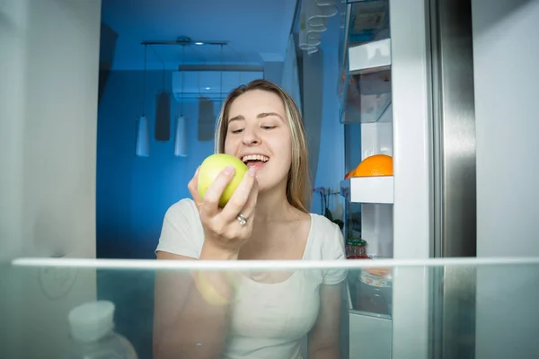 Młoda kobieta szczęśliwa biorąc jabłko lodówki. — Zdjęcie stockowe