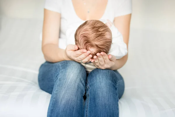 Mamma sitter på sängen och hålla huvudet av hennes 3 månader gammal baby — Stockfoto