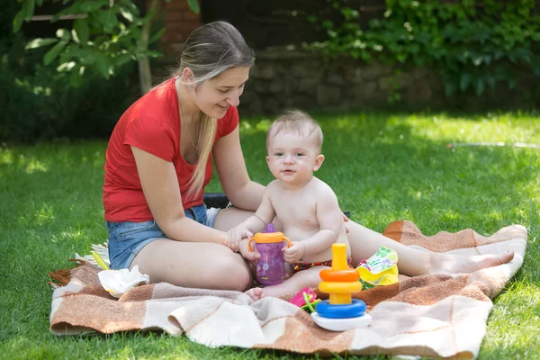 Молода мати годує свого маленького хлопчика на пікніку в парку — стокове фото
