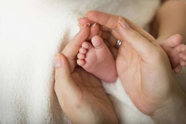 Primer plano de la madre cariñosa sosteniendo los pequeños pies del bebé recién nacido — Foto de Stock