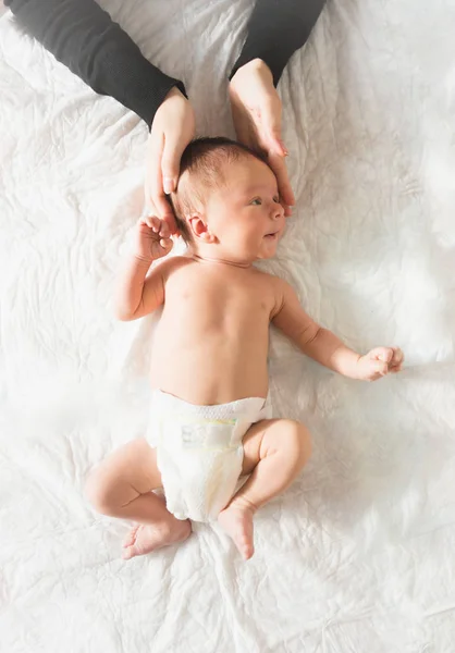 Mödrar händer håller barnets huvud liggande på sängen — Stockfoto