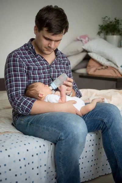年轻父亲坐在床上和喂养他新生的儿子 — 图库照片