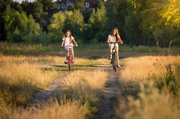 Duas meninas adolescentes andando de bicicleta no prado ao pôr do sol — Fotografia de Stock