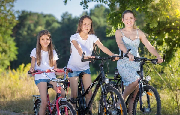 Portret dwóch siostra na rowerze z matki na łące nad jeziorem — Zdjęcie stockowe