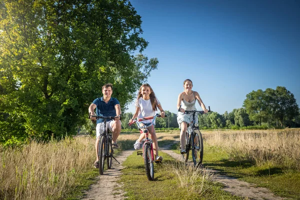 Familia alegre con hija montando bicicletas en el prado en soleado — Foto de Stock