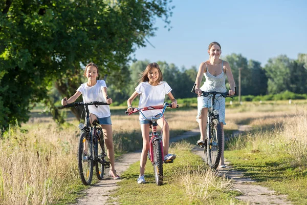 Happy young mother riding on bicycles with two daughters