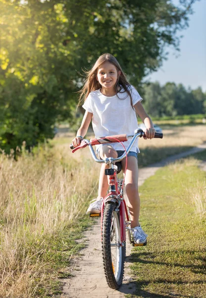 Wesoła dziewczyna z długimi włosami, jazdy na rowerze na polnej drodze w — Zdjęcie stockowe