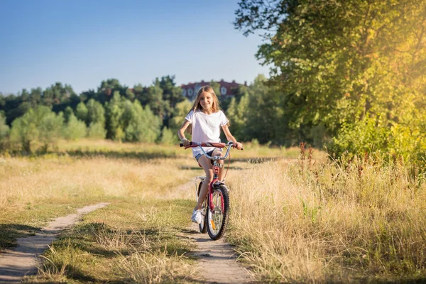 Счастливая молодая девушка на велосипеде на лугу в солнечный день — стоковое фото