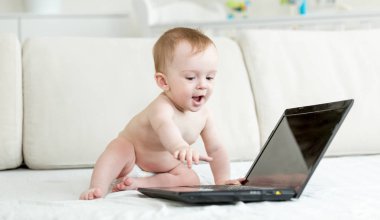 Yatağın üstüne oturan ve dizüstü bilgisayar kullanarak bezli bebek