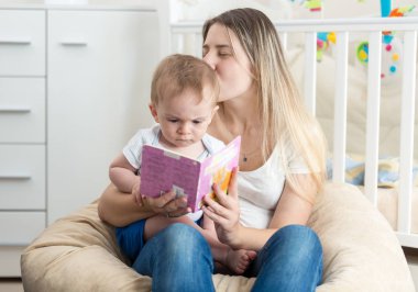 Güzel gülümseyen anne puf içinde oturan ve kitap okuma 