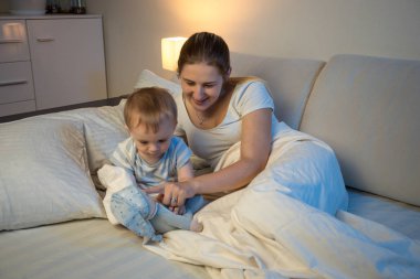 Gülümseyen anne bebeğini gece ve p yatakta yatan ile oynarken