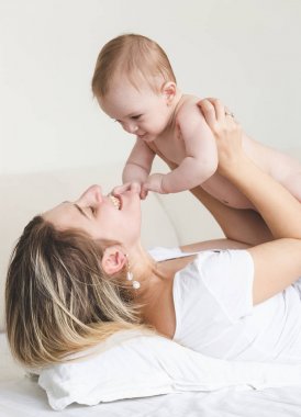 Mutlu genç annesiyle yatağa oynayan bebek boy gülümseyerek