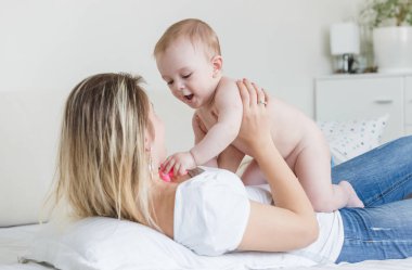 Yatakta yatarken ve bab ile oynarken mutlu genç anne portresi