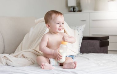 Erkek yatakta süt şişesi ile oturan sevimli bebek