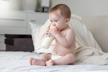 Yatağın üstüne oturan ve süt içmek güzel 9 aylık erkek bebek