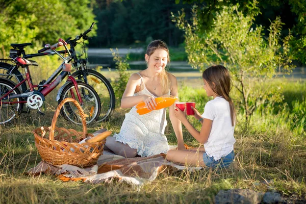 Feliz madre e hija bebiendo jugo de naranja en el picnic — Foto de Stock