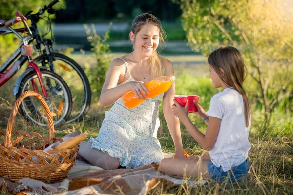 Young mother pouring juice from bottle into daughter's cup on pi — Stock Photo, Image