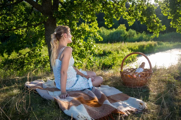 Jovem mulher sentada sob grande árvore no campo e olhando para o lago — Fotografia de Stock