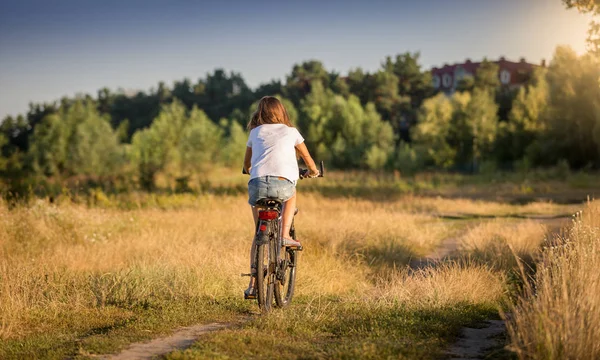 Hermosa chica en camiseta ciclismo en el prado al atardecer — Foto de Stock