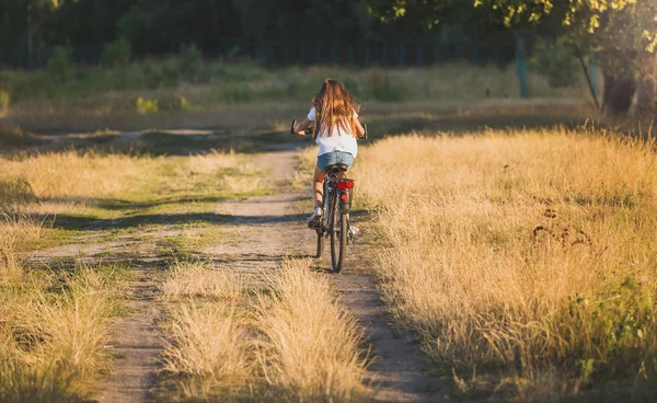 Woman riding bicycle on dirt road at meadow — Stock Photo, Image