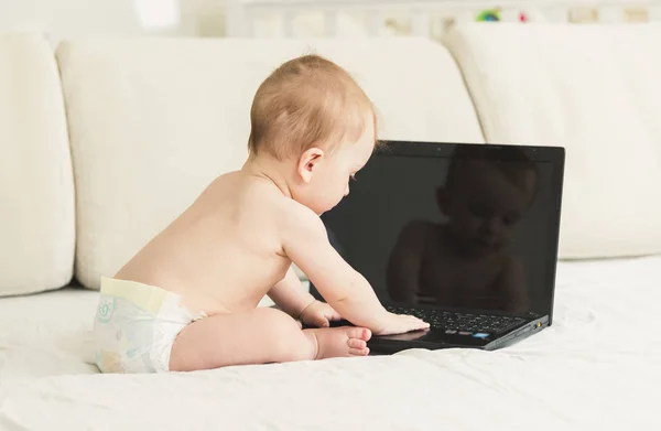 Bebé en pañales sentado en la cama y utilizando el ordenador portátil —  Fotos de Stock