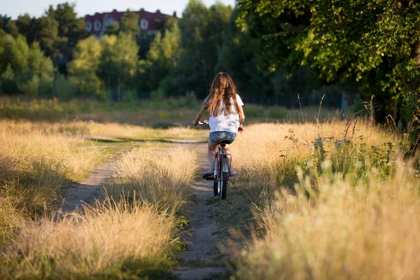 Beautiful girl riding bike at fields at sunset — Stock Photo, Image