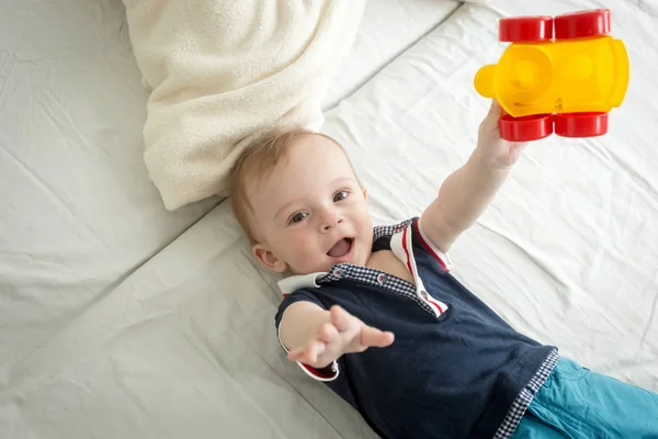 Веселый мальчик сидит на кровати и играет с игрушкой — стоковое фото