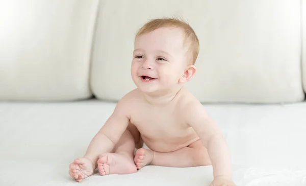 可爱微笑着 10 个月大的男婴，坐在沙发上的尿布 — 图库照片