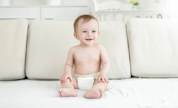 Joyeux bébé garçon souriant en couches assis sur le lit dans la chambre — Photo