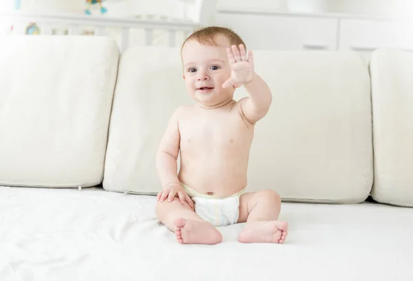 Leende pojke i blöjorna sitter på sängen — Stockfoto