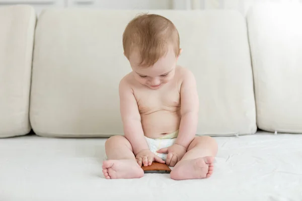 Baby pojke sitter på sängen och hålla smartphone — Stockfoto