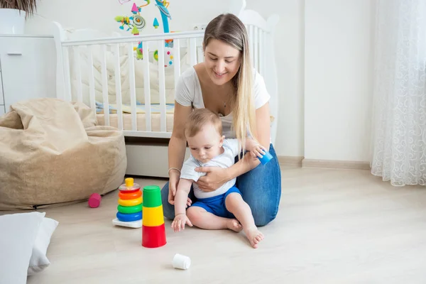 Mãe olhando para seu bebê menino montando pirâmide de brinquedos no chão um — Fotografia de Stock