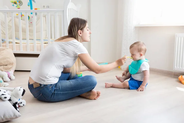 Mamma sitter på golvet i vardagsrummet och matar sitt barn med — Stockfoto