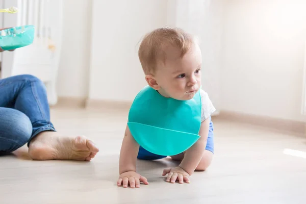 Cute baby boy in apron crawling on floor while mother trying to — Stock Photo, Image