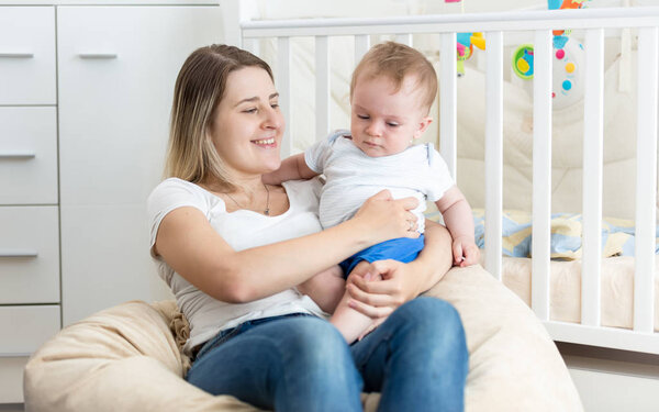 Cheerful young mother reading book to her baby boy at living roo