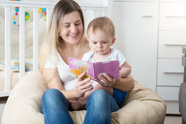 Schöne junge Mutter hält Baby auf dem Schoß und liest Buch — Stockfoto