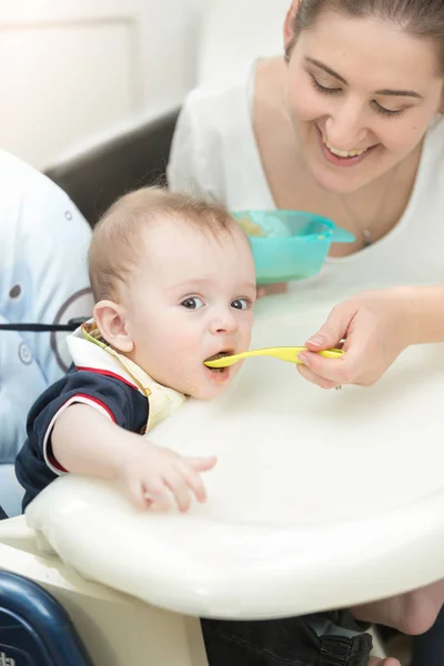 Sonriente joven madre alimentando a su bebé en silla alta —  Fotos de Stock