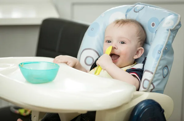 Sonriente niño sentado en silla alta y comiendo papilla de spoo —  Fotos de Stock
