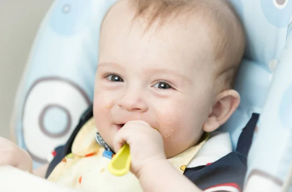 Szczęśliwy uśmiechający się dziecko jedzenia w krzesełko do karmienia w kuchni — Zdjęcie stockowe