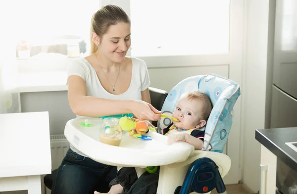 Madre alimentando a su hijo de 9 meses sentado en silla de niño — Foto de Stock