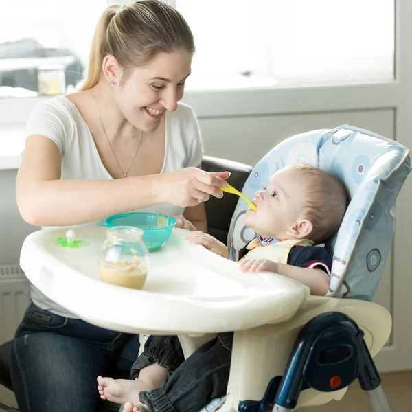 Красива усміхнена мати годує дитину на кухні — стокове фото