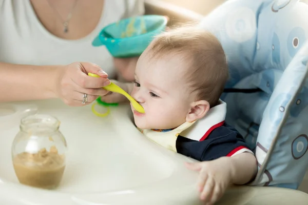 Young mother feeding her baby in highchair — Stock Photo, Image