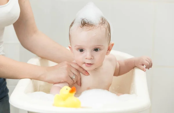 Niño jugando en baño de espuma con pato de goma amarillo — Foto de Stock