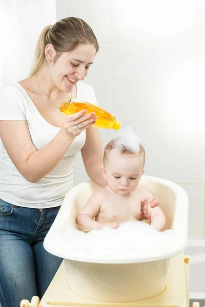 Sonriente madre joven lavando la cabeza de su bebé con champú — Foto de Stock