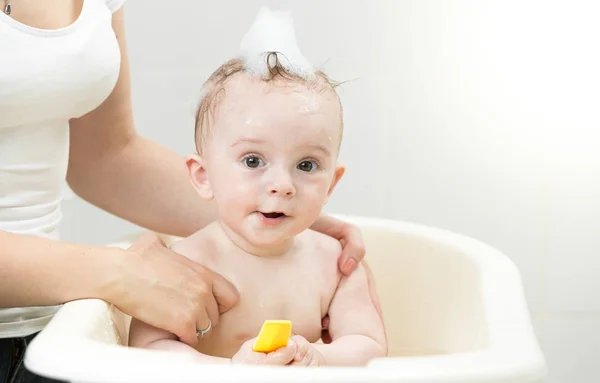 Милый мальчик играет в пенной ванне с желтой резиновой уткой — стоковое фото