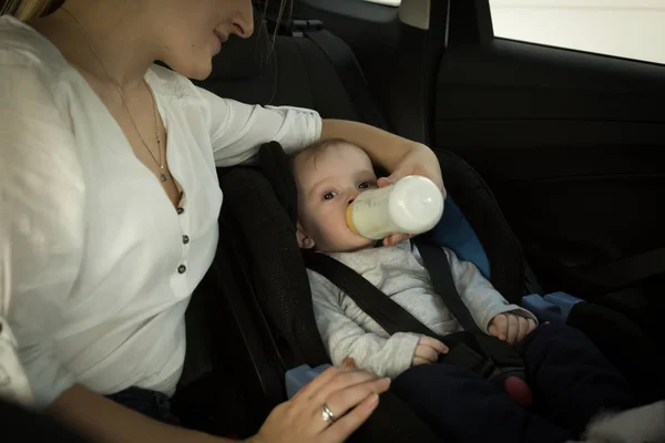 Joven madre dando leche en botella a su pequeño hijo en coche — Foto de Stock