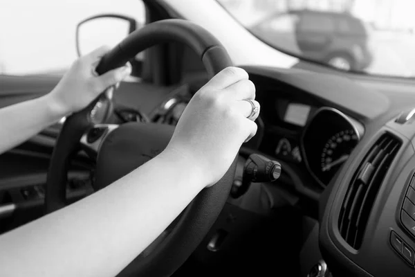 Closeup black and white image of woman holding car steering whee — Stock Photo, Image