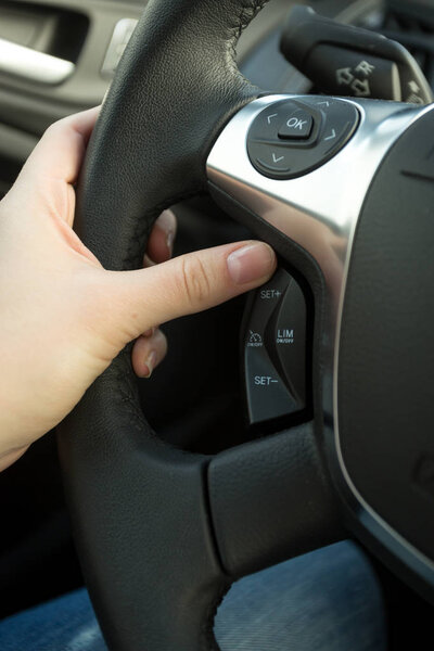Closeup of female driver adjusting cruise control system on stee