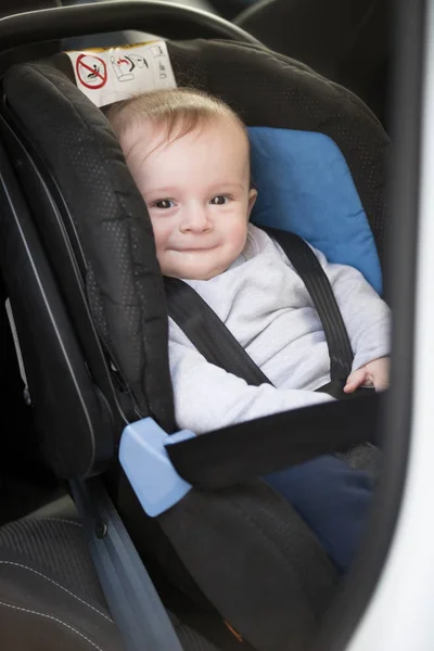 Lindo niño sonriente sentado en asiento de niño de coche — Foto de Stock